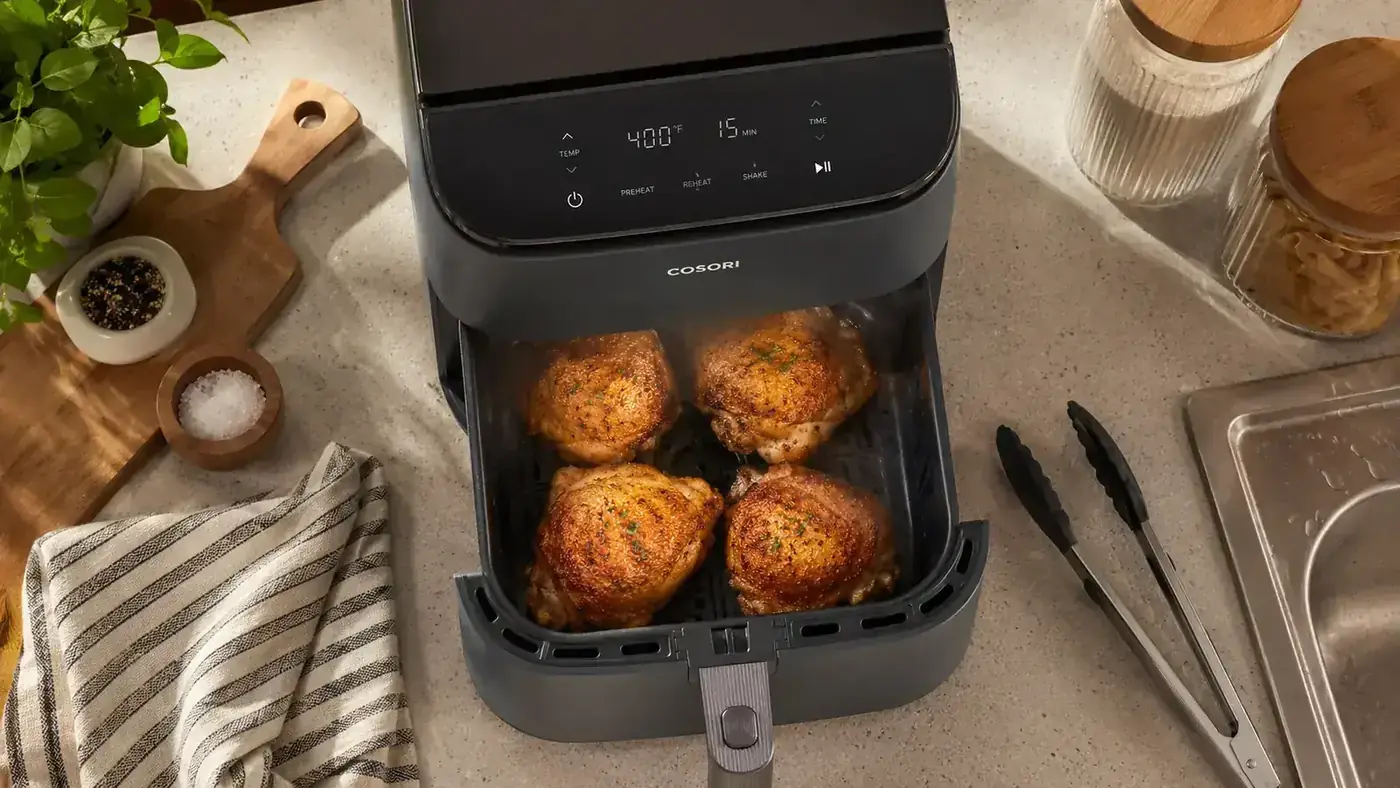 Hands pulling out the Cosori air fryer basket filled with golden crispy chicken thighs