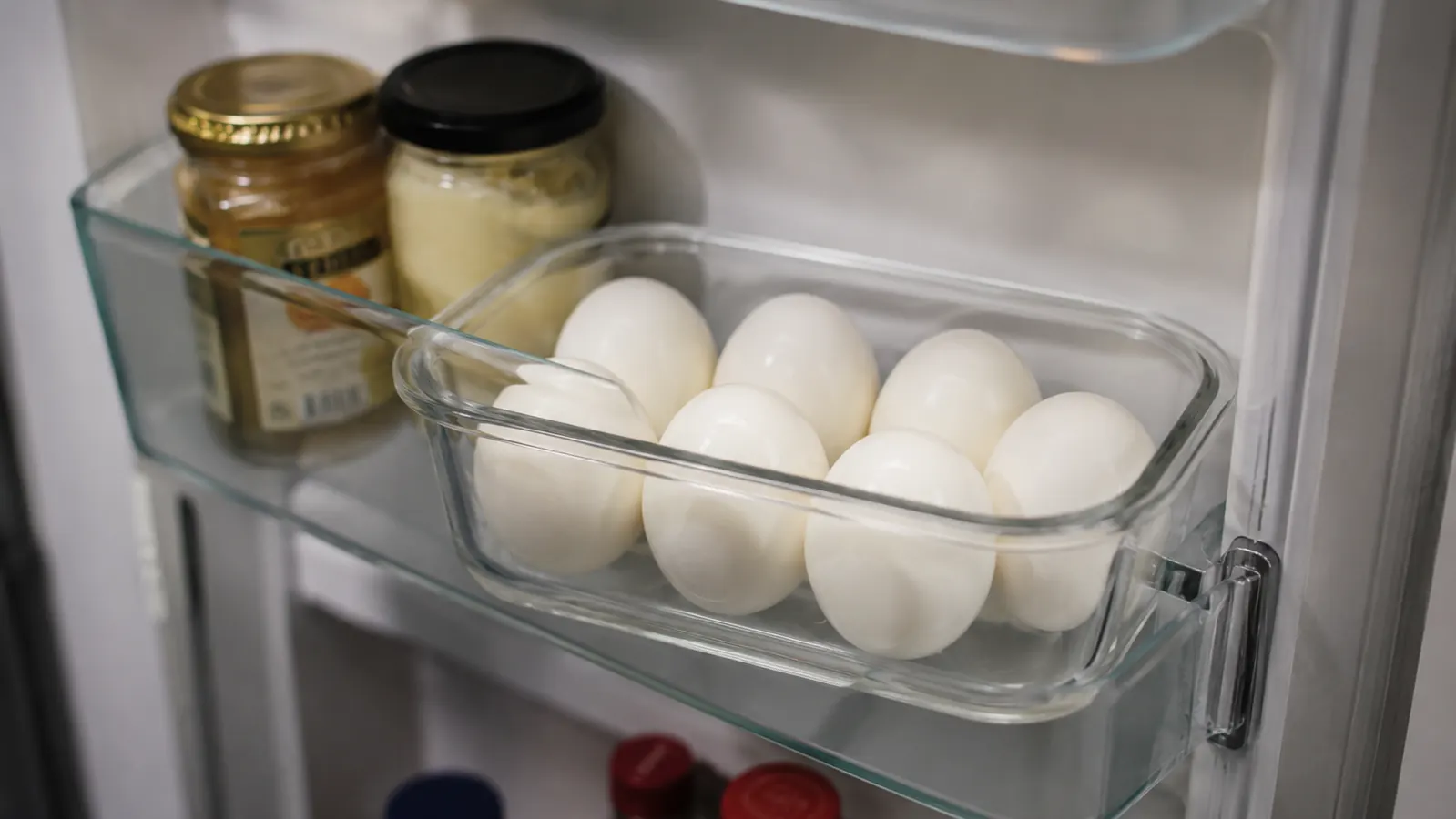 Six hard-boiled eggs in a glass meal prep container in a refrigerator door shelf
