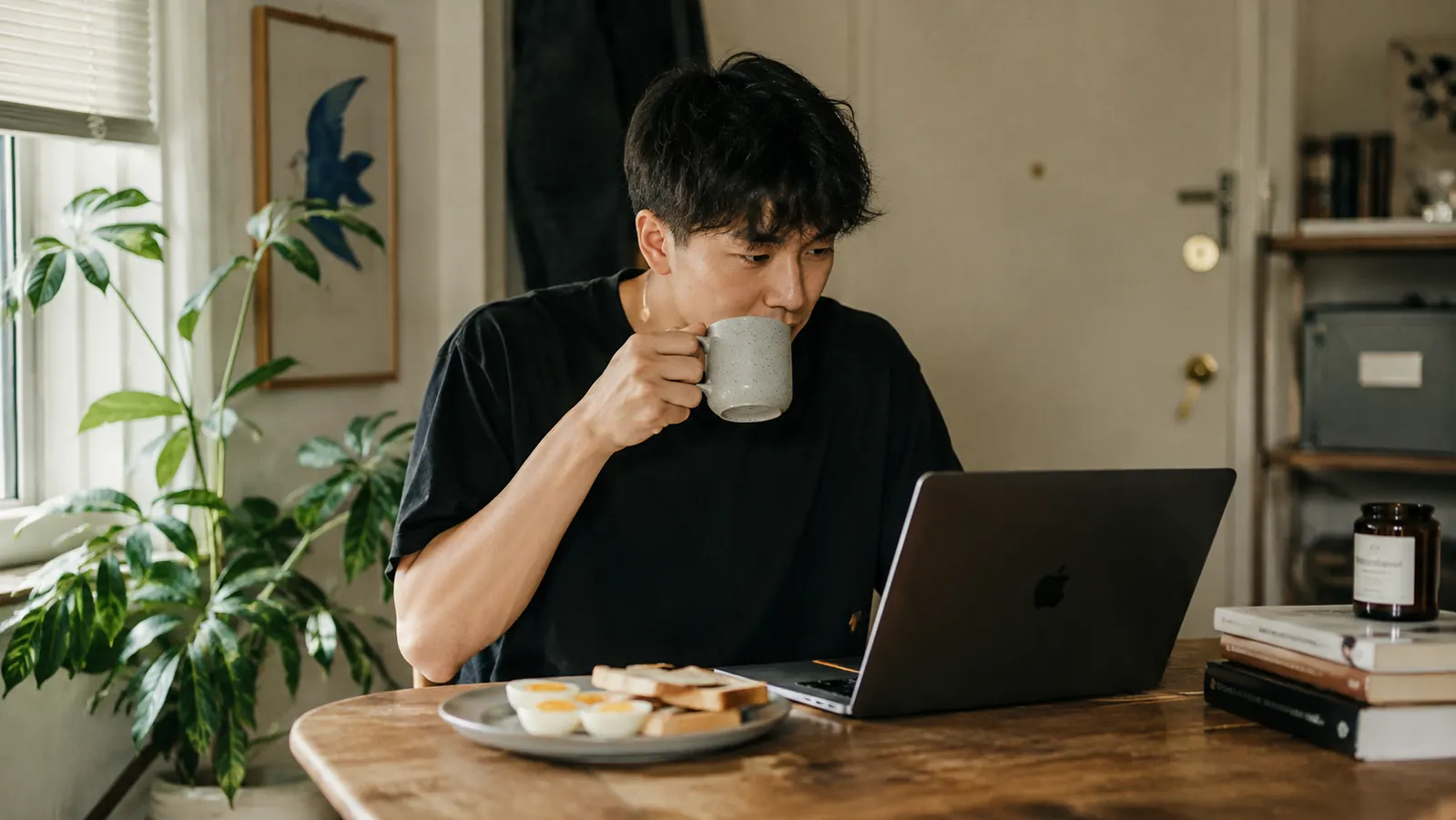 Person eating a quick egg breakfast at a small apartment dining table with a laptop open, ready for the work day