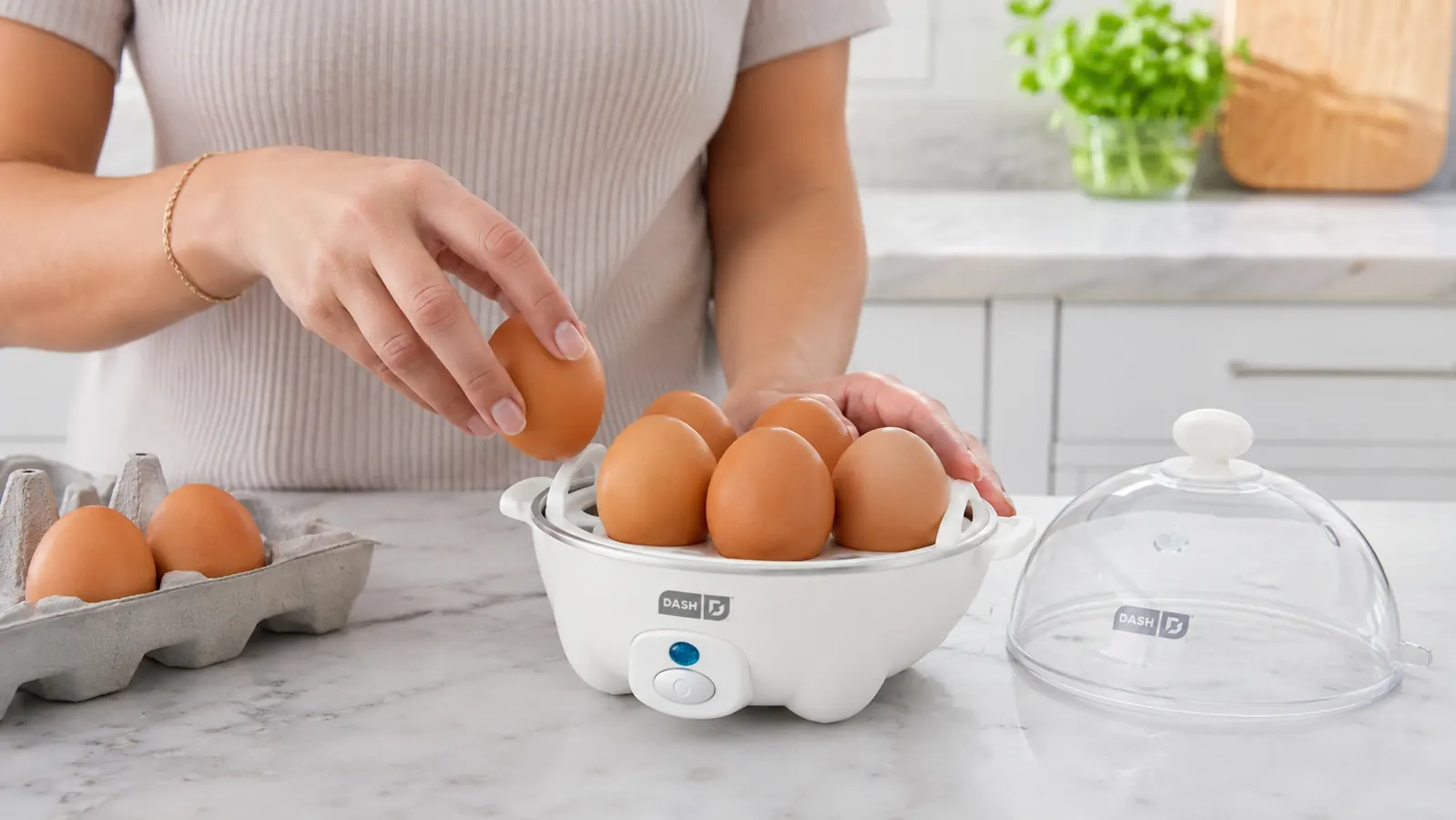 Hand placing eggs into the Dash Rapid Egg Cooker tray with the lid off