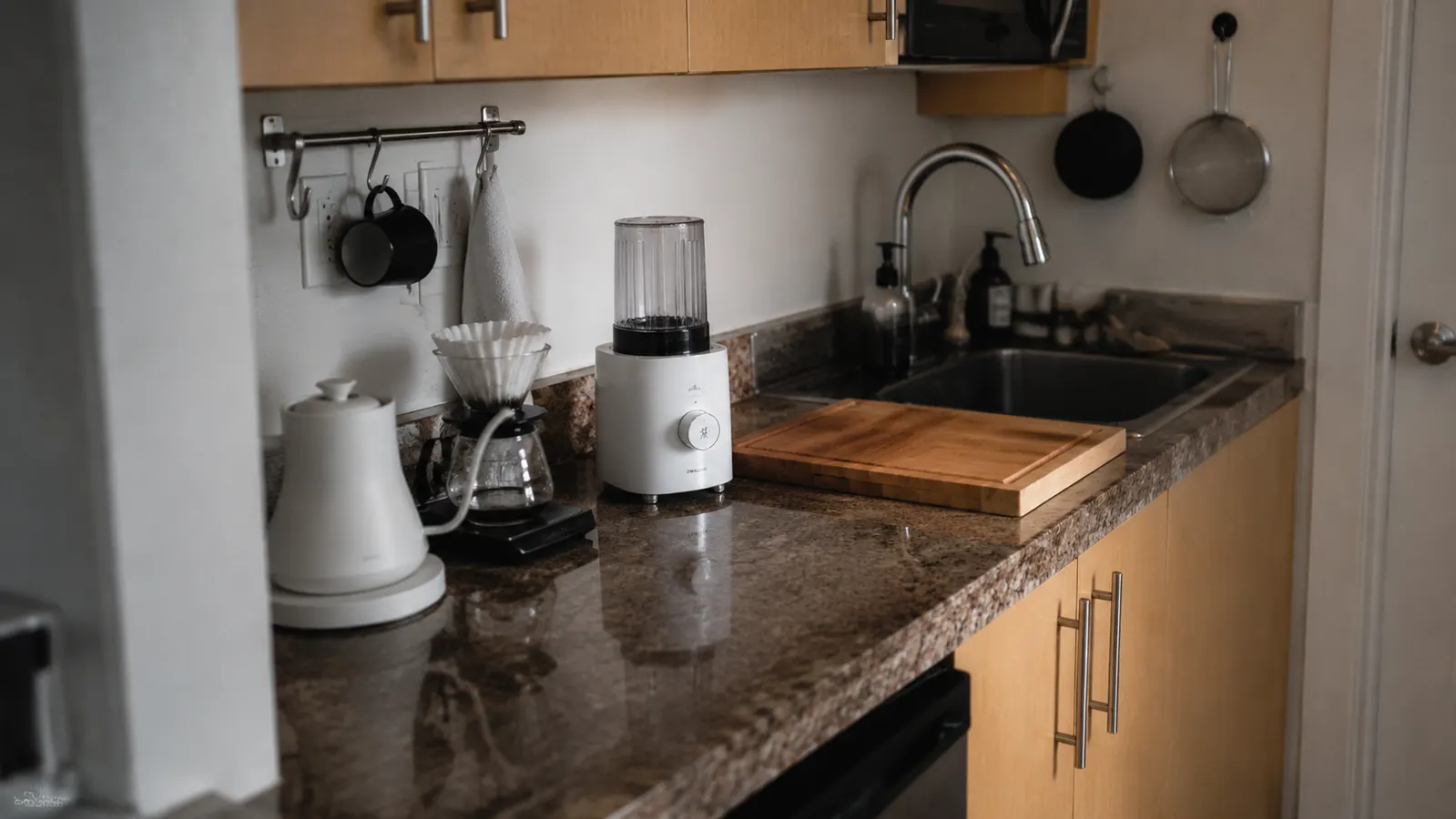 Small galley kitchen counter with a compact kettle next to a pour-over coffee setup and a single-serve blender