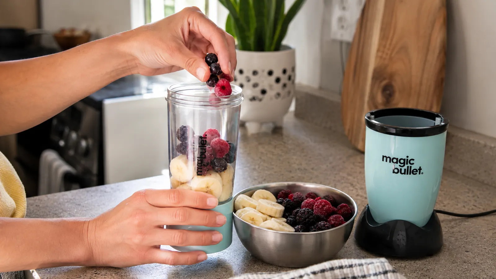 Hand placing frozen fruit into the Magic Bullet blender cup before blending