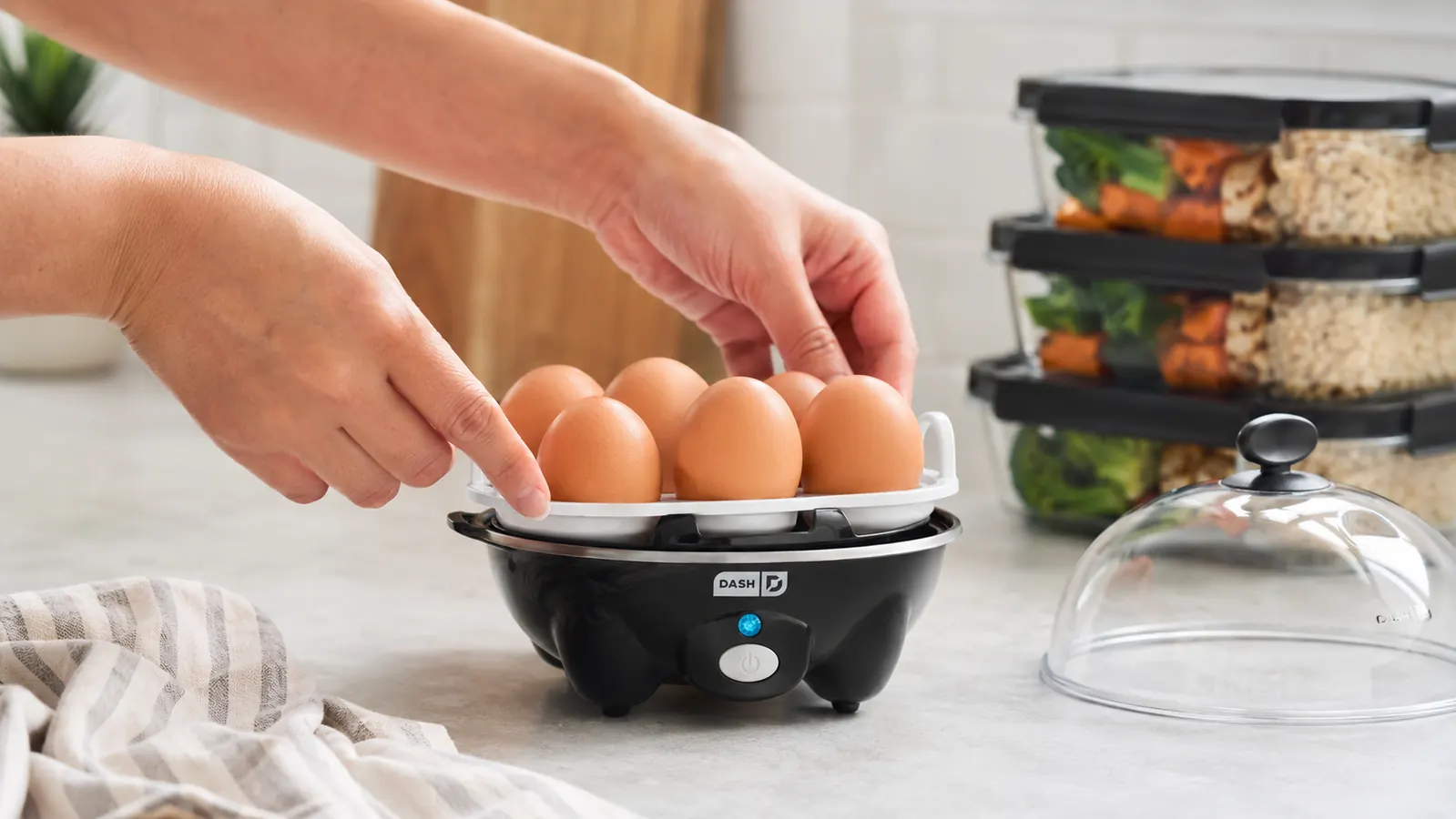 Hand placing eggs into the Dash Rapid Egg Cooker tray before a meal prep session