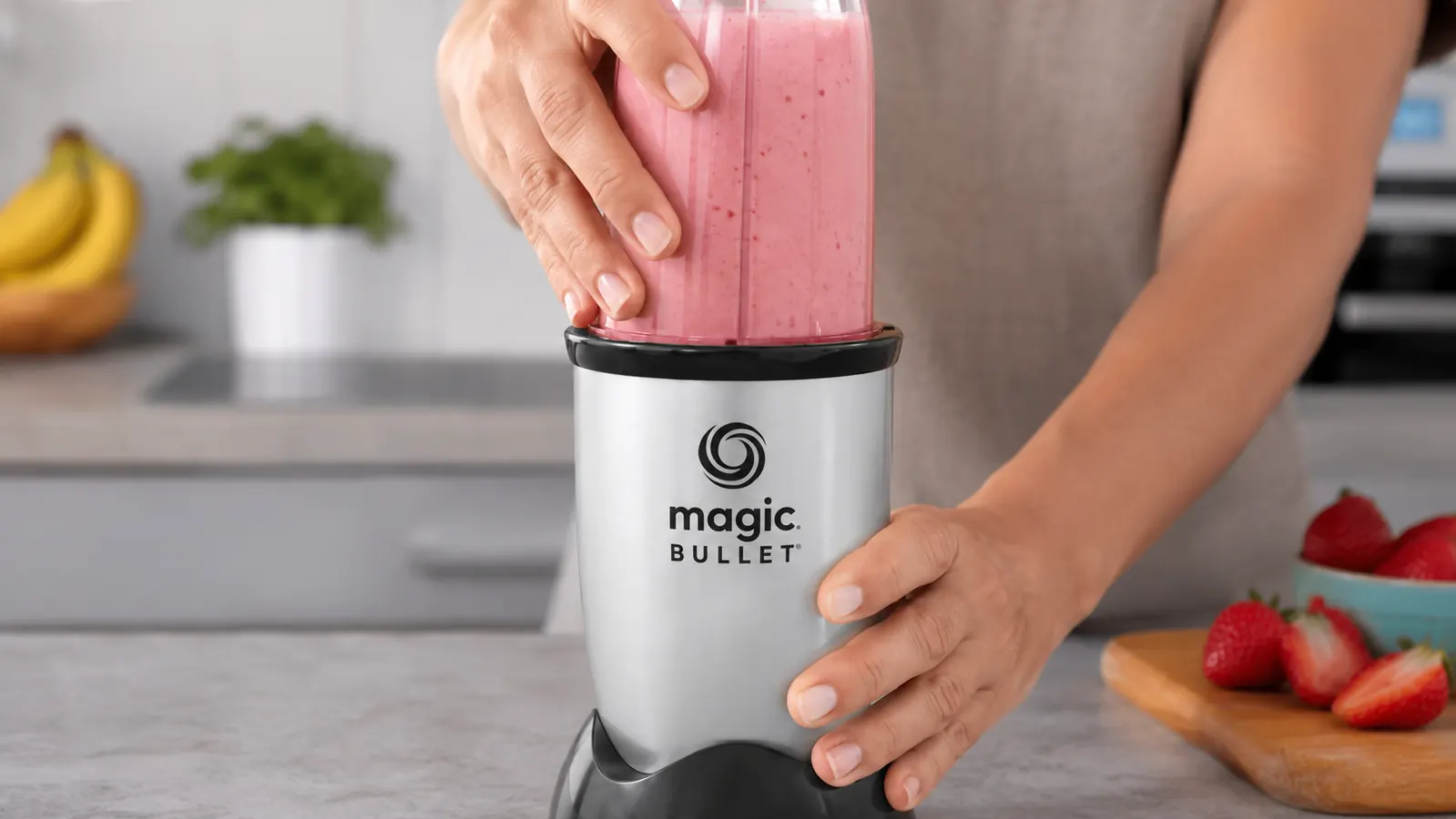 Hand attaching the blade cup to the Magic Bullet motor base with a smoothie visible inside