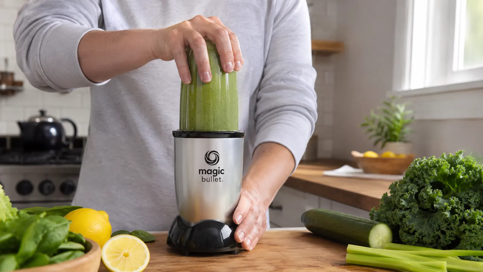 Hand twisting a Magic Bullet cup onto the base to blend a green smoothie