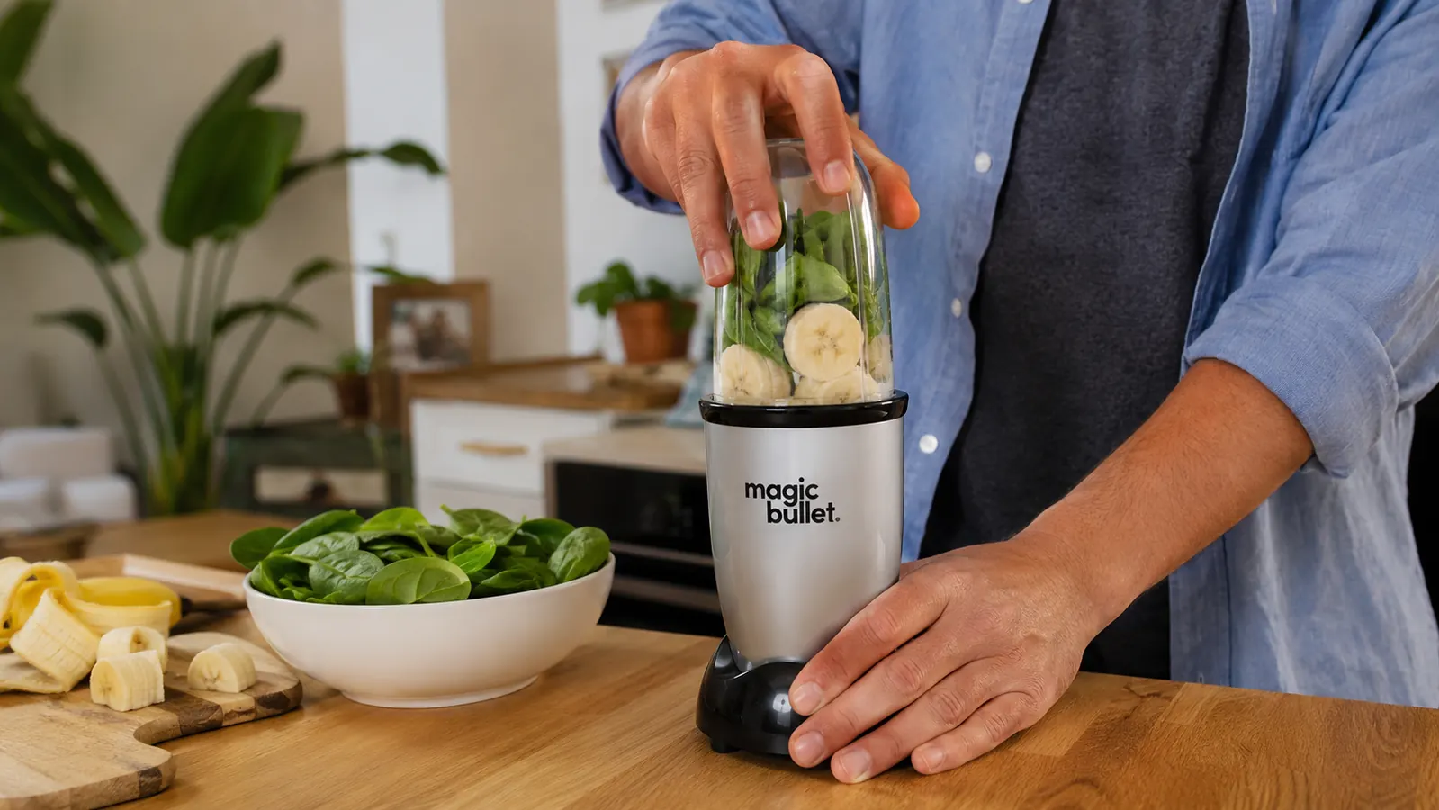 Hand attaching a Magic Bullet blending cup to the base on a countertop next to a banana and some spinach