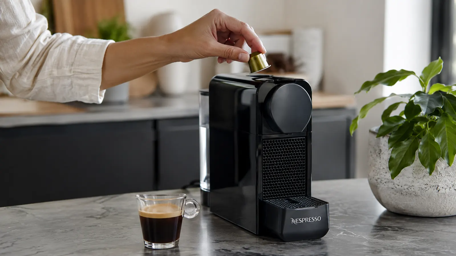 Hand inserting an Original-line espresso capsule into a Nespresso Essenza Mini machine
